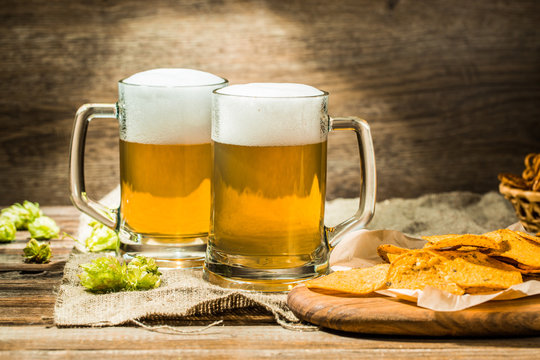 Couple beer mug with hop and chips on boards at linen cloth