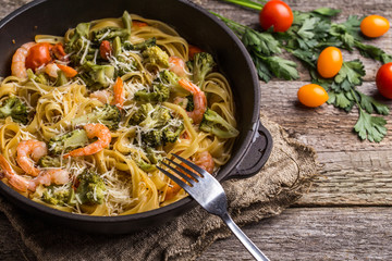 Pasta linguine with shrimps and broccoli in dripping pan on wooden background.