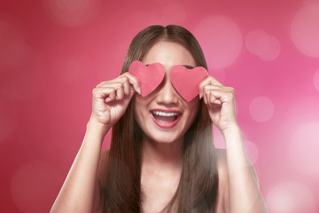 Smiling asian woman covering her eyes with red heart shape