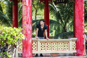 Fototapeta na wymiar Young handsome man standing in Chinese temple in Bangkok, Thailand. Horizontal outdoors shot