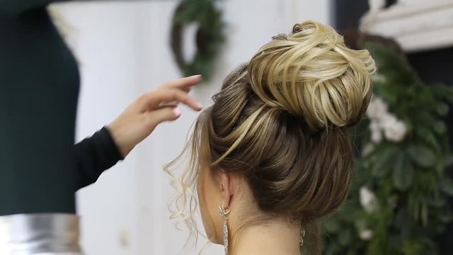 Hair stylist adds final touches to up do bun hairstyle of blonde woman in barber beauty salon