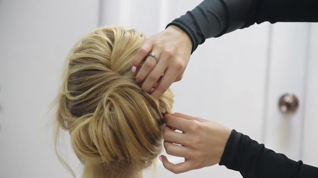 Closeup of hairdresser hands coiffeur makes beautiful hairstyle. Barber is finishing the final touches
