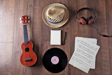 Guitar, headphones, music sheets and straw hat on wooden surface, top view