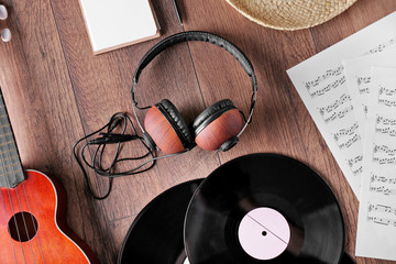 Small guitar, headphones, vinyl records and music sheets on wooden surface, top view