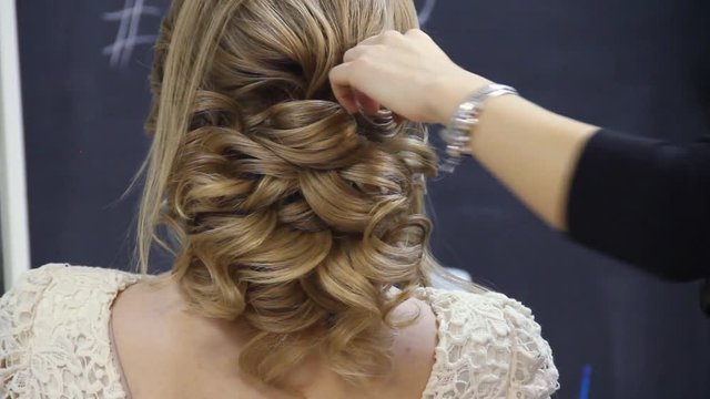 Closeup of hairdresser hands coiffeur makes beautiful hairstyle. Barber is finishing the final touches