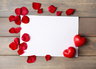 Paper greeting card with decorative hearts and rose petals on wooden background