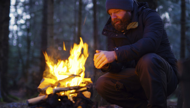 Man warms himself at camp fire in the forest