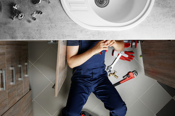 Male plumber repairing sink pipes in kitchen, top view - obrazy, fototapety, plakaty