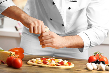 Male hands preparing pizza at wooden table closeup