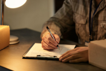 Courier making notes in delivery receipt at table