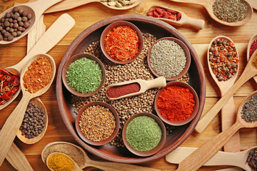 Different spices in bowls and spoons on wooden background