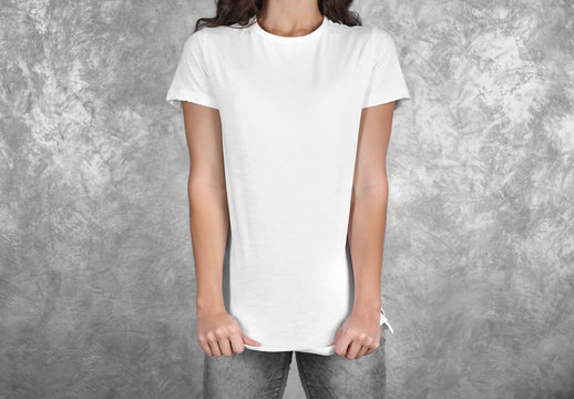 Young woman in blank white t-shirt standing against grey textured wall, close up