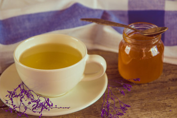 Green tea in a white cup and jar of honey with spoon and blue ki