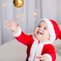 funny baby boy weared in Santa hat with golden Christmas ball