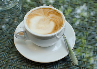 The cup of cappuccino on the glass surface.