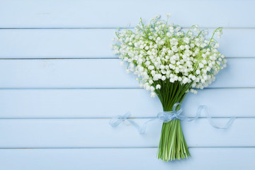 Beautiful bouquet of flowers lily of the valley on  blue wooden table from above.
