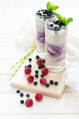 Two glasses with fresh blueberry smoothie decorated berries and mint leaves on white wooden background. Selective focus