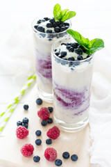 Two glasses with fresh blueberry smoothie decorated berries and mint leaves on white wooden background. Selective focus