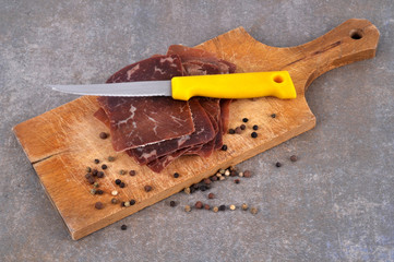 Tranches de viande des Grisons sur une planche à découper avec un couteau et des baies