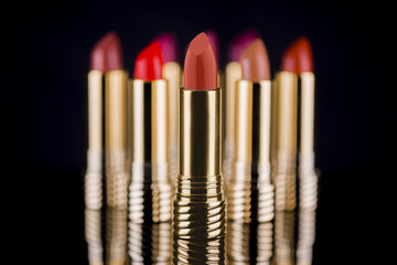 Several lipstick color samples on golden luxury tube, first sharp and the other blurred with nice reflection on black background