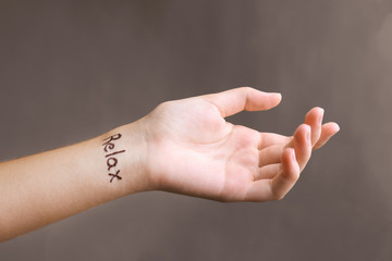Female hand with tattoo word RELAX on grey background