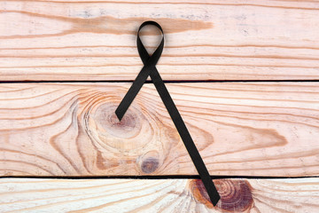 Black ribbon on wooden background. Melanoma and mourning concept
