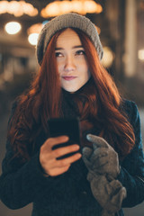 Young woman with read hair standing at the street and using mobile phone. 