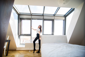 Woman standing near the window while stretching near bed