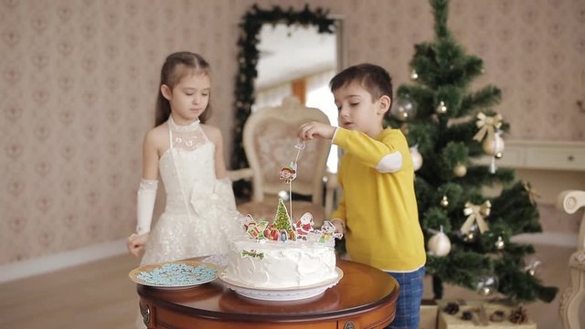 little brother and sister decorate Christmas cake. beautiful children in a spacious and bright room near the Christmas tree