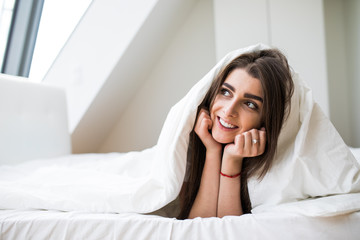 Smiling woman under a duvet in her bedroom