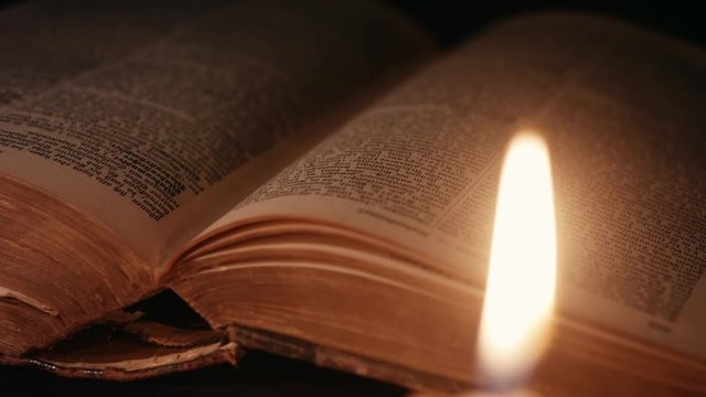 static shot of an open ancient book lit by candles