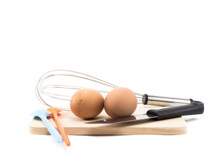 two eggs and whisk and orange, blue spoon and knife on wood square isolated on white background