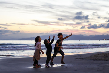 Fototapeta premium Silhouette of three kids playing on the beach at sunset.