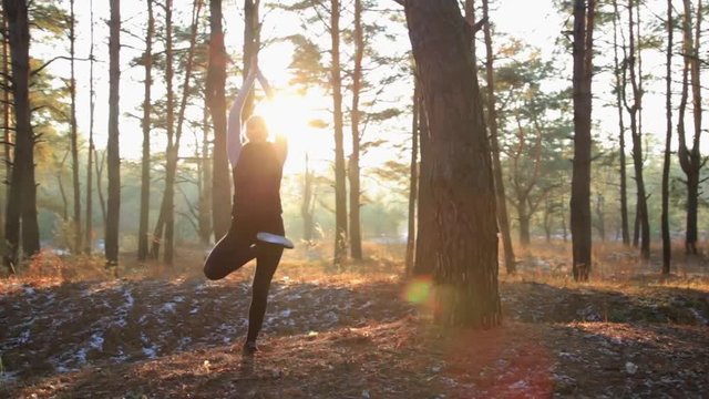 Sporty woman doing yoga breathing exercises with her hands together and her eyes closed in a serene forest at sunset. Healthy lifestyle concept.
