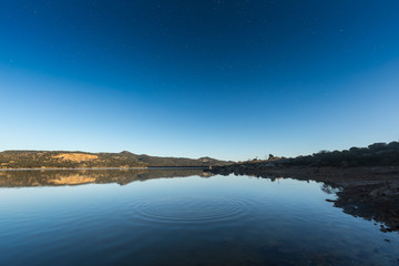 Ripples on a lake at sunrise with star filled deep blue sky