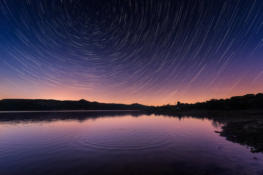 Star trails above ripples on a calm lake in Corsica at sunrise