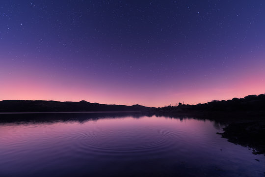 Ripples on a lake at sunrise with star filled purple sky