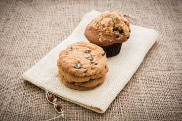 Stacked chocolate chip cookies and cupcakes on brown napkin over