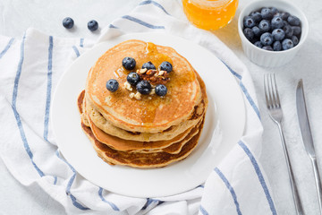 Stack of pancakes with fresh blueberries, nuts and honey on white plate. Healthy breakfast food.