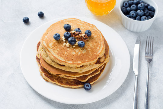 Stack of homemade corn pancakes with blueberries, walnuts and honey on white plate. Healthy breakfast food