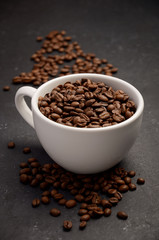 Natural organic roasted coffee beans in white cup on black background, selective focus, vertical.