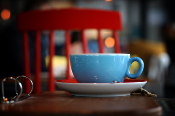 Blue cup of coffee on a wooden table with a red chair in the background