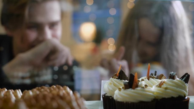 Beautiful couple of young people in a candy store. A girl and a guy in a sweater choose Cake and desserts for themselves. Showcase pleasantly decorated. The girl with long hair, brunette.