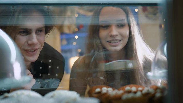 Beautiful couple of young people in a candy store. The girl and the guy chosen Cake and desserts for themselves. Showcase pleasantly decorated