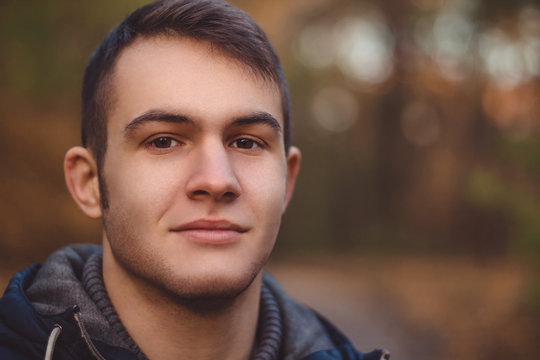 The guy looks at the camera and smiles sweetly. Close-up shot. The autumn weather outside.
