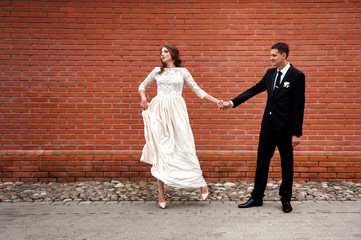 Obraz na płótnie Canvas Newlyweds embracing next to red brick wall. Young wedding couple.