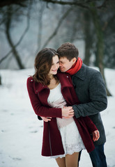 Man tenderly embraces beautiful girl.They stand on a snow-covered meadow at a huge tree.Scenic winter walk in Park.A romantic feeling.Fantastic shooting.Fashionable toning.Creative color.