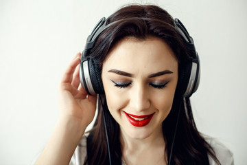 Fototapeta premium Happy pretty smiling woman with red lips listens to music in headphones over white background