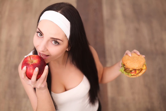 healthy woman smelling hamburger and holding apple