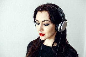 Happy pretty smiling woman with red lips in a black jacket listens to music in headphones over white background